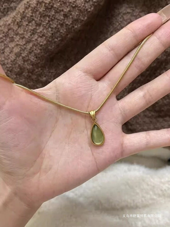 Gold-tone green crystal teardrop pendant necklace held in hand