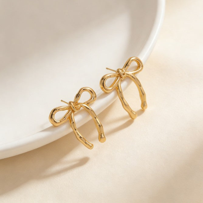 Gold sculpted bow earrings displayed on a white dish