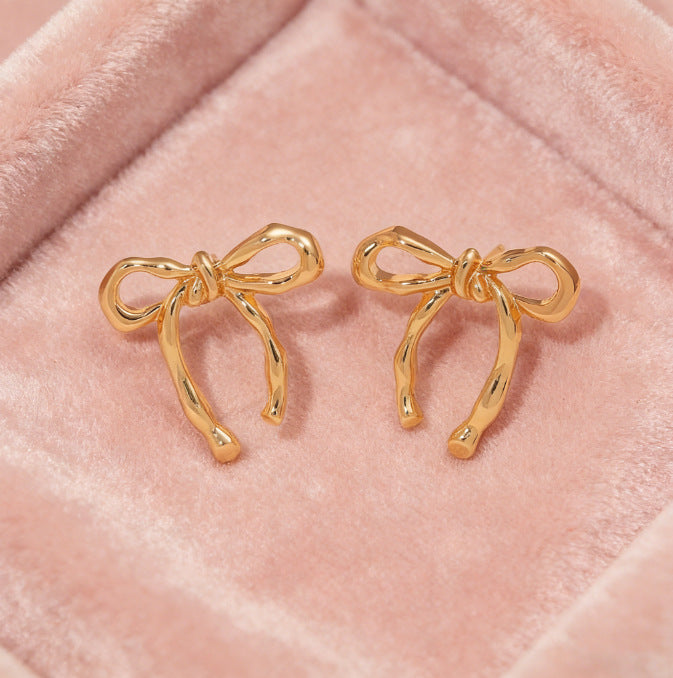 Pair of gold bow earrings on soft pink fabric