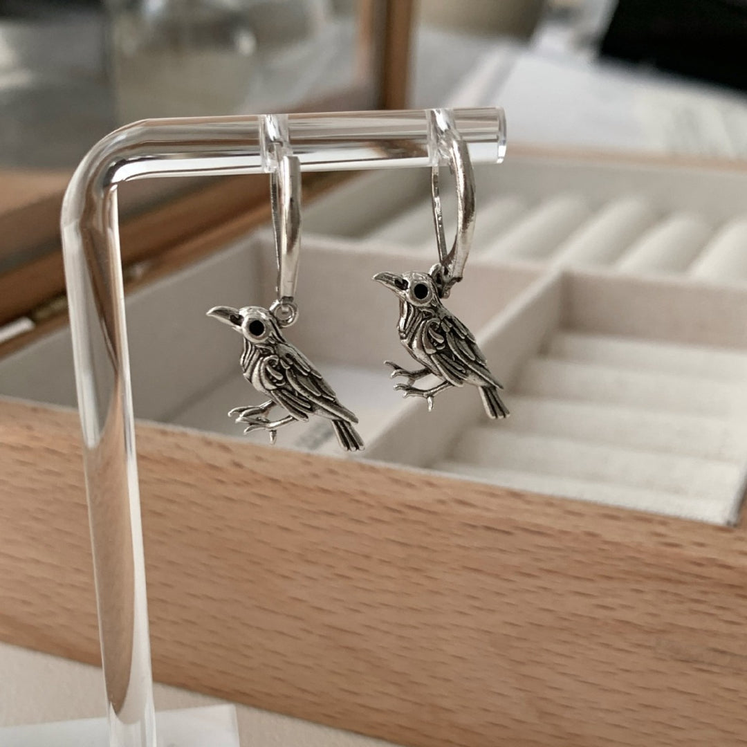 Vintage raven earrings hanging on a display stand