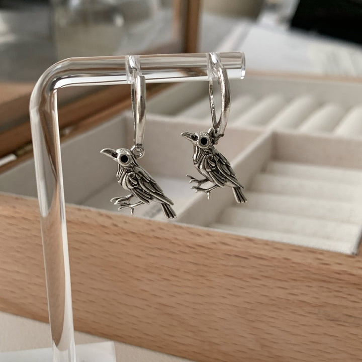 Vintage raven earrings hanging on a display stand